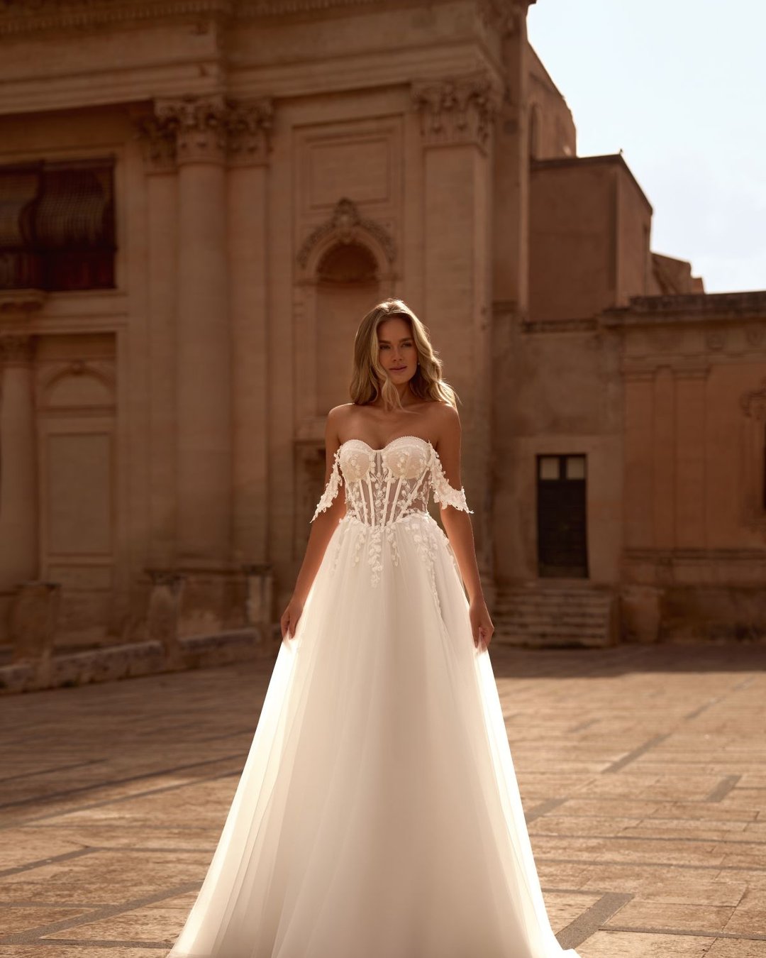 Model Krasyva to romantyczna i niezwykle kobieca suknia ślubna o kroju A-line, która zachwyca swoją delikatnością i subtelnym wykończeniem. Wykonana z lekkiego tiulu, miękko otula sylwetkę, tworząc lekką i zwiewną kompozycję idealną na każdy typ ceremonii – od plenerowego ślubu po elegancką uroczystość w pałacowych wnętrzach.