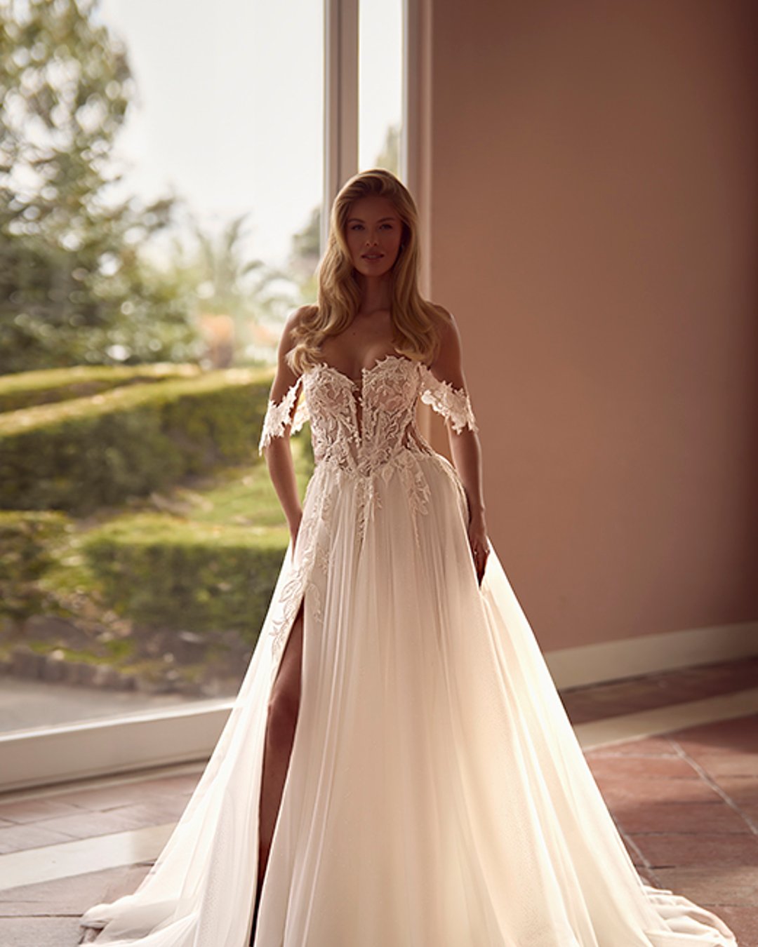 Zmysłowa, romantyczna i pełna lekkości – suknia Virinea to połączenie klasycznej princesski z nowoczesnym charakterem. Transparentny gorset z opadającymi ramiączkami pięknie eksponuje dekolt i ramiona, a delikatna spódnica z tiulu z rozcięciem subtelnie odsłania nogę. Idealna dla Panny Młodej, która marzy o bajkowej, ale wyrazistej stylizacji.