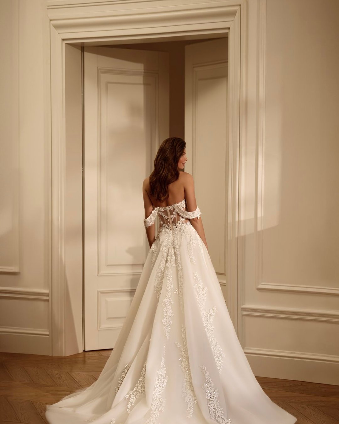 Suknia o linii A, zachwycająca swoją delikatnością i romantycznym charakterem. Gorsetowa góra wykonana z transparentnego tiulu, ręcznie zdobiona misteryjną koronką w motywy roślinne. Przezroczyste boki optycznie modelują sylwetkę, pięknie ją podkreślając.