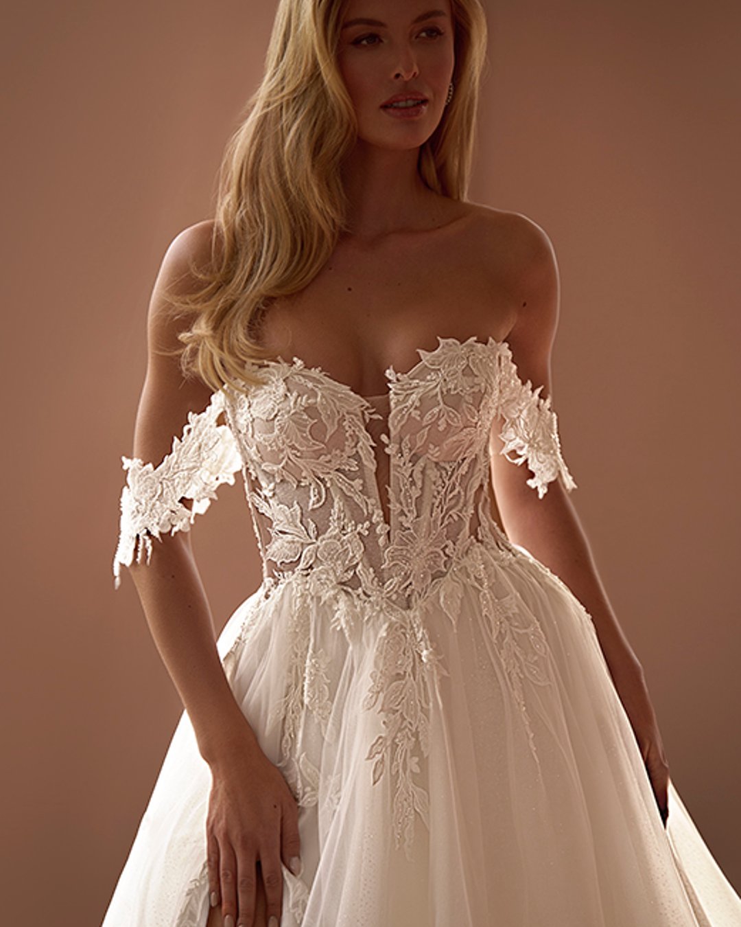 Zmysłowa, romantyczna i pełna lekkości – suknia Virinea to połączenie klasycznej princesski z nowoczesnym charakterem. Transparentny gorset z opadającymi ramiączkami pięknie eksponuje dekolt i ramiona, a delikatna spódnica z tiulu z rozcięciem subtelnie odsłania nogę. Idealna dla Panny Młodej, która marzy o bajkowej, ale wyrazistej stylizacji.