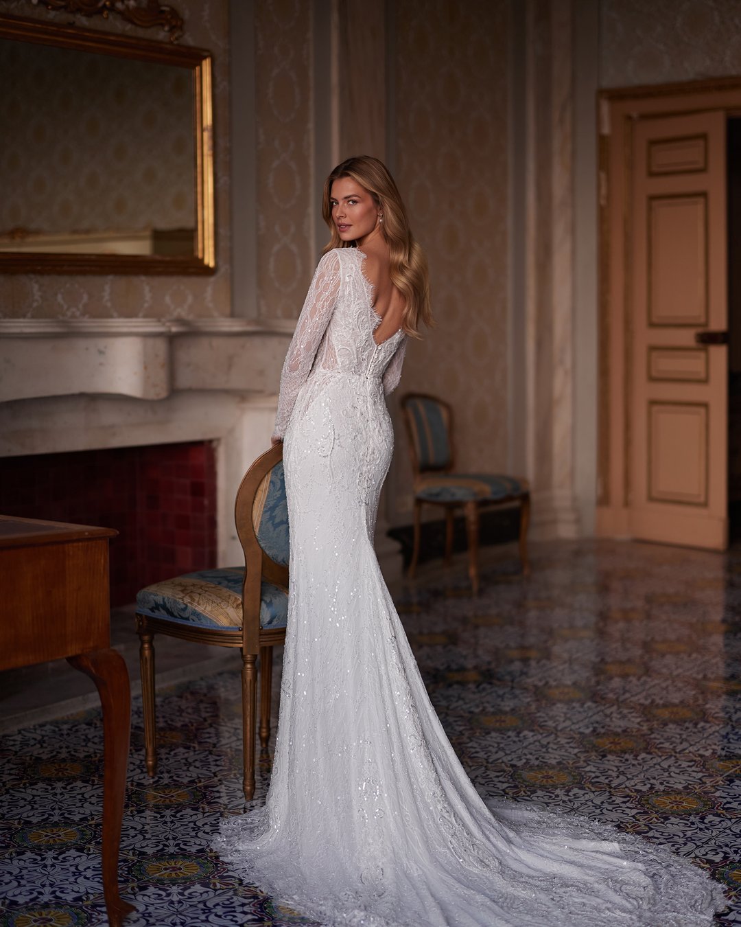 Oto sukienka Andarella z kolekcji AnnaSposa – esencja elegancji i romantyzmu. Jej dekolt w kształcie litery V oraz długie rękawy zdobione francuską koronką podkreślają wyjątkowy charakter, a dopasowany krój z trenem sprawia, że każda panna młoda poczuje się jak prawdziwa królowa w tym blasku. Przezroczystości i subtelne detale nadają całości niepowtarzalnego uroku, idealnie wpisując się w wymarzone wesele.