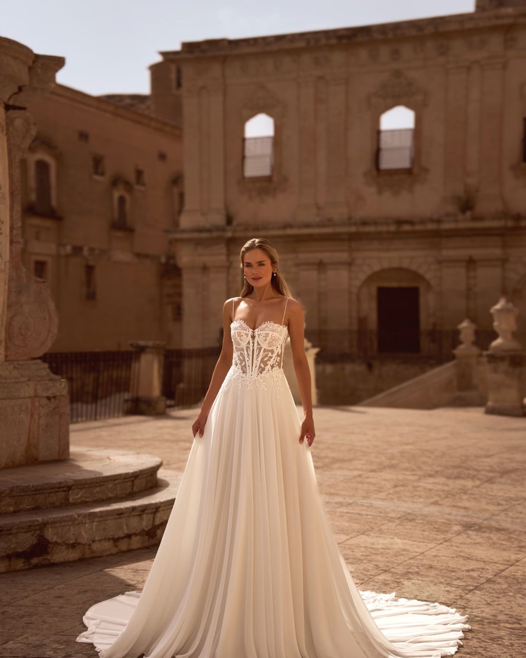 Model Bogdana to romantyczna suknia ślubna o kroju A-line, wykonana z niezwykle lekkiego i zwiewnego muślinu, który pięknie układa się w ruchu. Jej delikatność idzie w parze z elegancją i kobiecością, tworząc stylizację idealną zarówno na ślub w plenerze, jak i elegancką uroczystość w pałacowym stylu.