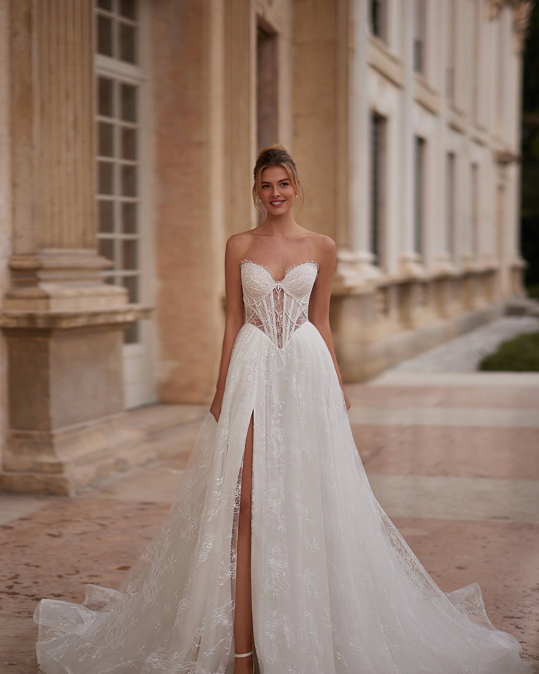 Suknia Kaviella z kolekcji AnnaSposa to połączenie elegancji i nowoczesności, które zachwyci każdą pannę młodą. Wykonana z delikatnej francuskiej koronki, z zmysłowym rozporkiem i gorsetowym krojem, subtelnie podkreśla sylwetkę, a przezroczyste szerokie ramiączka dodają jej lekkości. Uzupełniona o bolerko i efektowny tren, ta suknia sprawi, że poczujesz się wyjątkowo w najważniejszym dniu swojego życia.