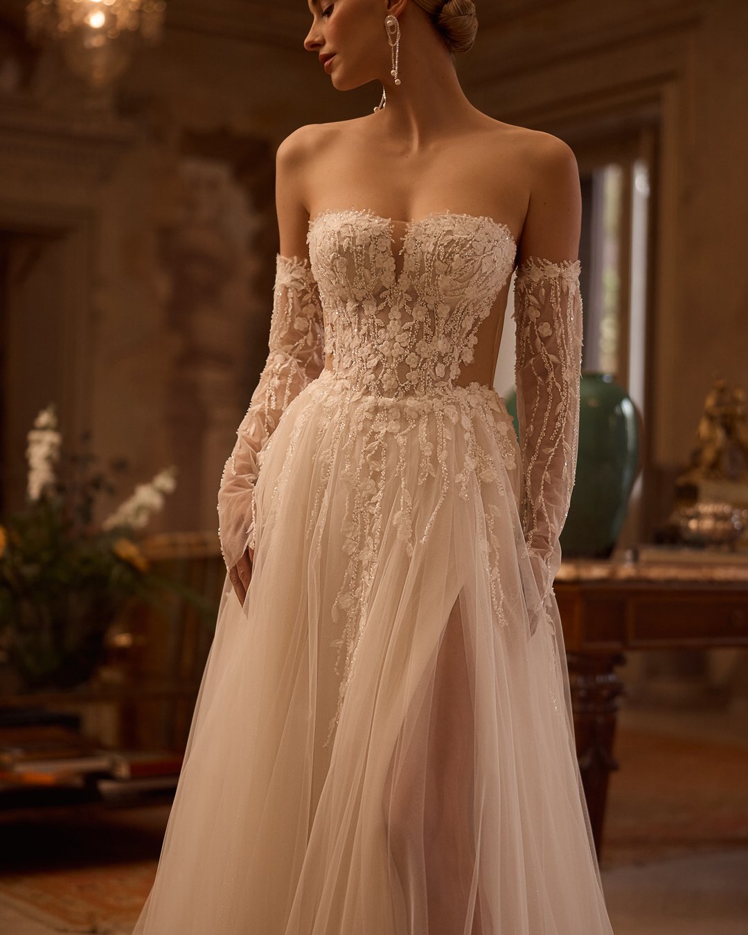 Suknia ślubna 5831 z kolekcji Elizabeth Passion łączy nowoczesny design z romantycznym wyrafinowaniem. Przezroczysta góra ozdobiona delikatną koronką i kwiatowymi aplikacjami, w połączeniu z szeroką, tiulową spódnicą, tworzy niepowtarzalny efekt, który zachwyca blaskiem. Nakładane rękawy dodają całości subtelności, sprawiając, że każda panna młoda poczuje się jak prawdziwa królewna w tym wyjątkowym dniu.