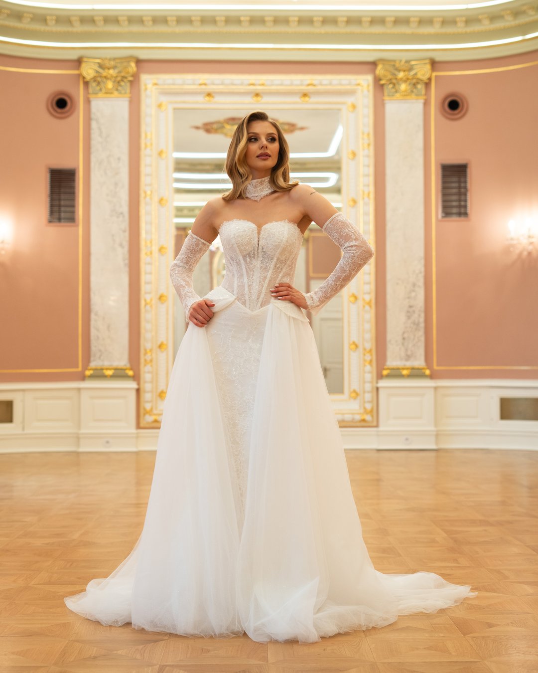 Suknia ślubna Bianca z kolekcji LaLiven to doskonałe połączenie klasyki i nowoczesności, które zachwyca swoją elegancją. Dwuczęściowa konstrukcja w kształcie tuby, ozdobiona francuską koronką i subtelnym trenem, podkreśla sylwetkę, a efektowne nakładane rękawki oraz choker dodają jej wyjątkowego charakteru. Dzięki wąskiej baskince i lśniącemu wykończeniu, Bianca sprawi, że każda panna młoda poczuje się jak prawdziwa gwiazda w dniu swojego ślubu.