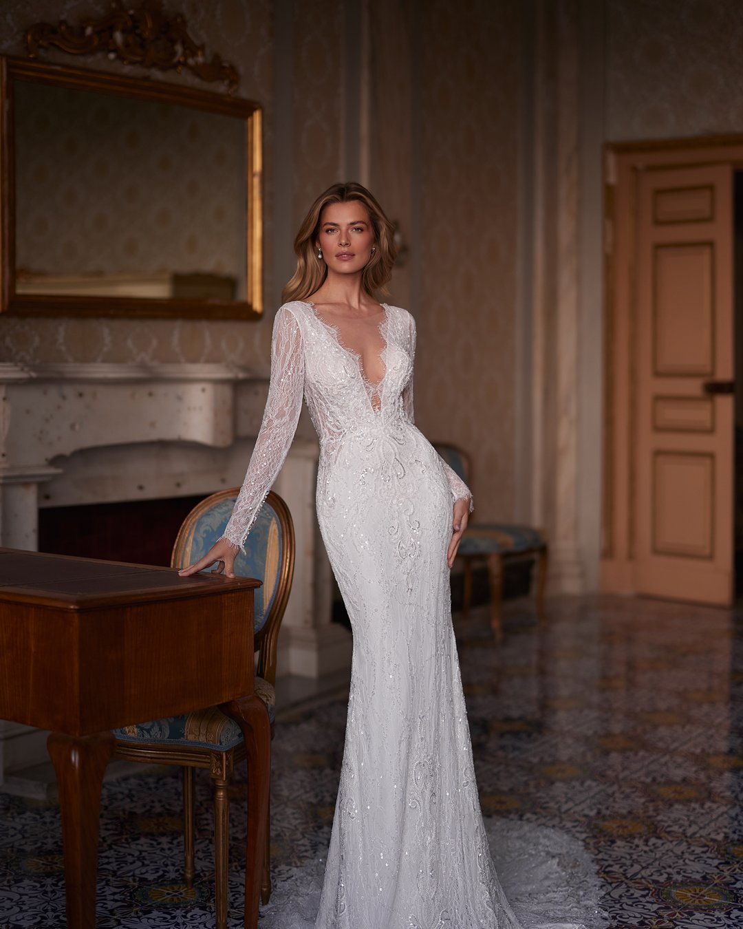 Oto sukienka Andarella z kolekcji AnnaSposa – esencja elegancji i romantyzmu. Jej dekolt w kształcie litery V oraz długie rękawy zdobione francuską koronką podkreślają wyjątkowy charakter, a dopasowany krój z trenem sprawia, że każda panna młoda poczuje się jak prawdziwa królowa w tym blasku. Przezroczystości i subtelne detale nadają całości niepowtarzalnego uroku, idealnie wpisując się w wymarzone wesele.