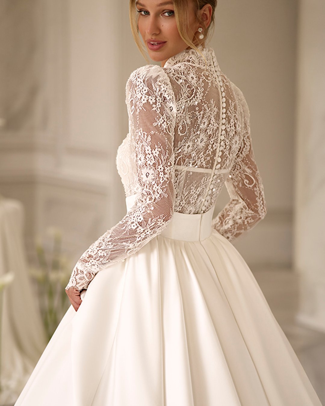 Calayra od Anna Sposa to elegancka suknia ślubna typu princessa, która zachwyca zmysłowym dekoltem w kształcie litery V, długimi koronkowymi rękawami oraz olśniewającą, rozkloszowaną satynową spódnicą z trenem. To połączenie klasyki i nowoczesnej delikatności.