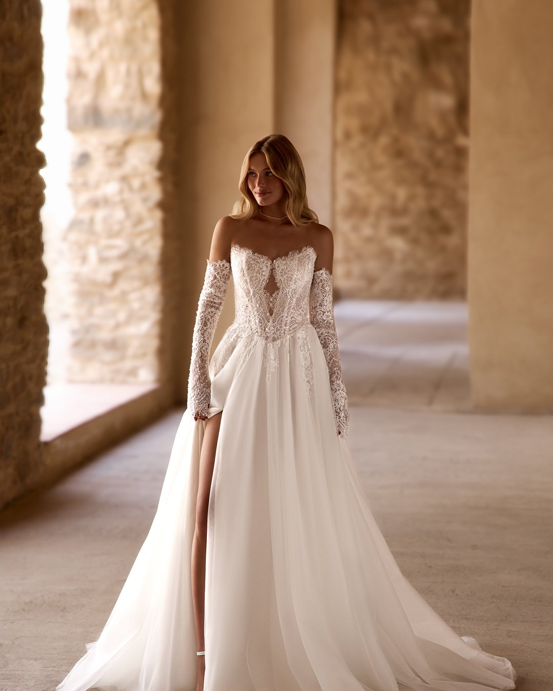 Suknia ślubna Forutina z kolekcji AnnaSposa to romantyczny wybór dla wyjątkowej panny młodej. Jej rozkloszowana linia A, zdobiona koronką francuską, zachwyca przezroczystymi detalami oraz efektownym trenem, natomiast gorsetowy krój z wyciętymi plecami podkreśla sylwetkę, a subtelny rozporek dodaje nuty zmysłowości. Dodatkowe, nakładane rękawy wprowadzają elegancję, sprawiając, że każda chwila w tej sukni będzie niezapomniana.