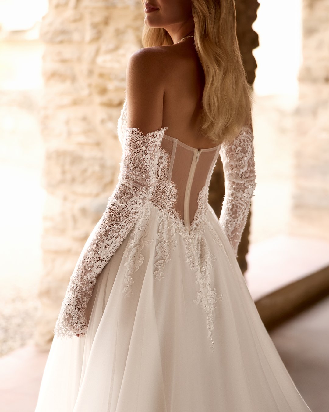 Suknia ślubna Forutina z kolekcji AnnaSposa to romantyczny wybór dla wyjątkowej panny młodej. Jej rozkloszowana linia A, zdobiona koronką francuską, zachwyca przezroczystymi detalami oraz efektownym trenem, natomiast gorsetowy krój z wyciętymi plecami podkreśla sylwetkę, a subtelny rozporek dodaje nuty zmysłowości. Dodatkowe, nakładane rękawy wprowadzają elegancję, sprawiając, że każda chwila w tej sukni będzie niezapomniana.