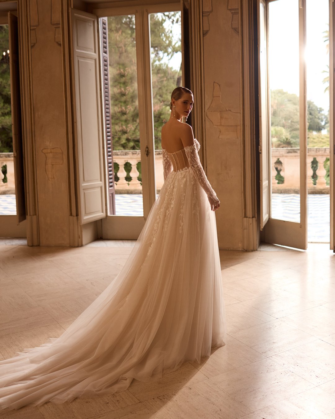 Suknia ślubna 5831 z kolekcji Elizabeth Passion łączy nowoczesny design z romantycznym wyrafinowaniem. Przezroczysta góra ozdobiona delikatną koronką i kwiatowymi aplikacjami, w połączeniu z szeroką, tiulową spódnicą, tworzy niepowtarzalny efekt, który zachwyca blaskiem. Nakładane rękawy dodają całości subtelności, sprawiając, że każda panna młoda poczuje się jak prawdziwa królewna w tym wyjątkowym dniu.