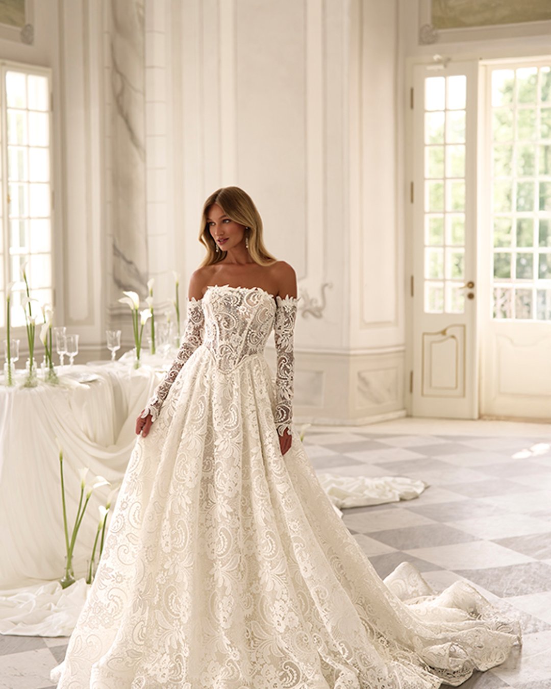 Suknia ślubna Bohnia od Anna Sposa to elegancka princeska z szeroką spódnicą i transparentnym gorsetem. Wykonana z bogato zdobionej gipiury, ozdobiona perłami, z prostym dekoltem i odpinanymi rękawami. Idealna dla panny młodej marzącej o bajkowym wyglądzie.