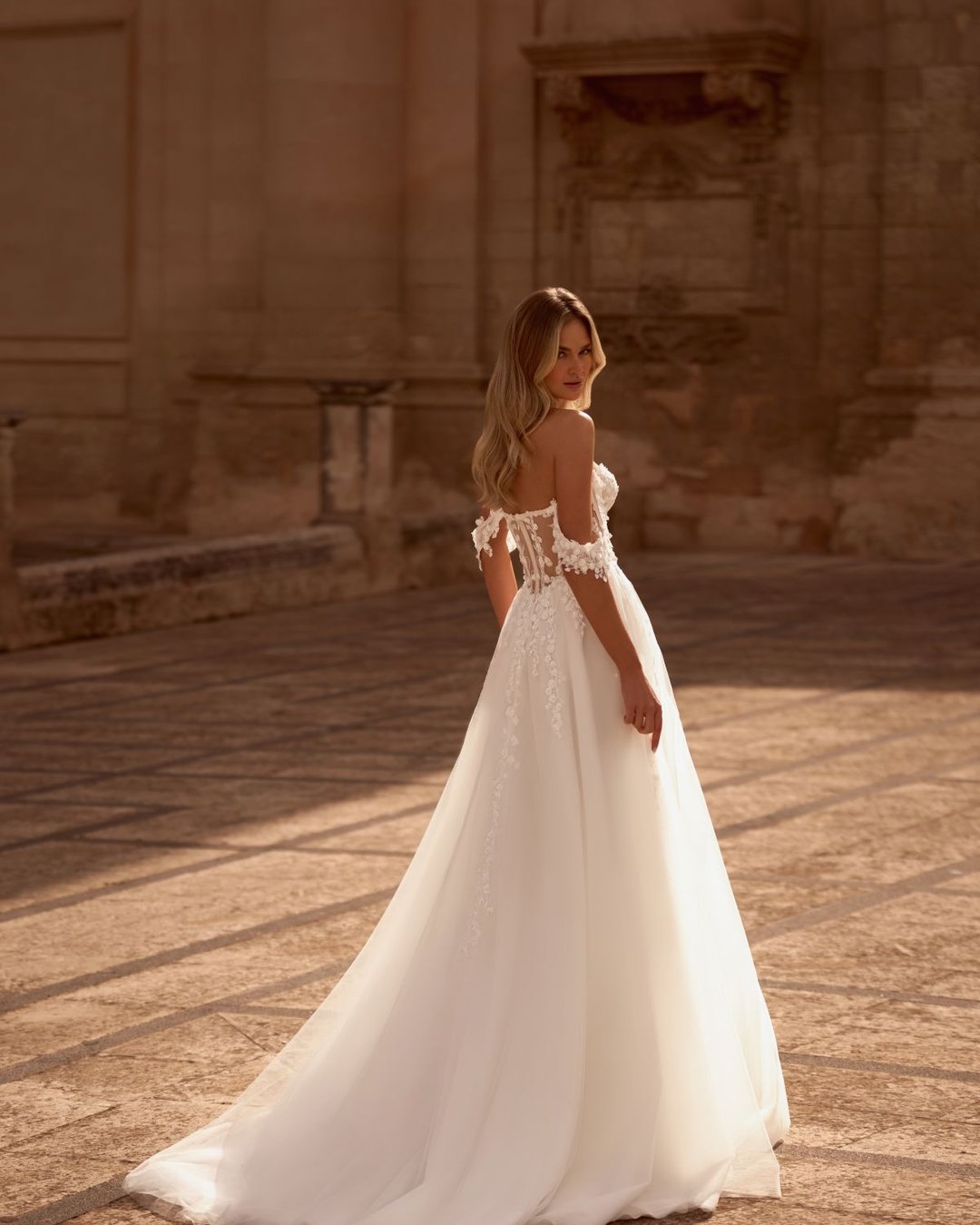 Model Krasyva to romantyczna i niezwykle kobieca suknia ślubna o kroju A-line, która zachwyca swoją delikatnością i subtelnym wykończeniem. Wykonana z lekkiego tiulu, miękko otula sylwetkę, tworząc lekką i zwiewną kompozycję idealną na każdy typ ceremonii – od plenerowego ślubu po elegancką uroczystość w pałacowych wnętrzach.