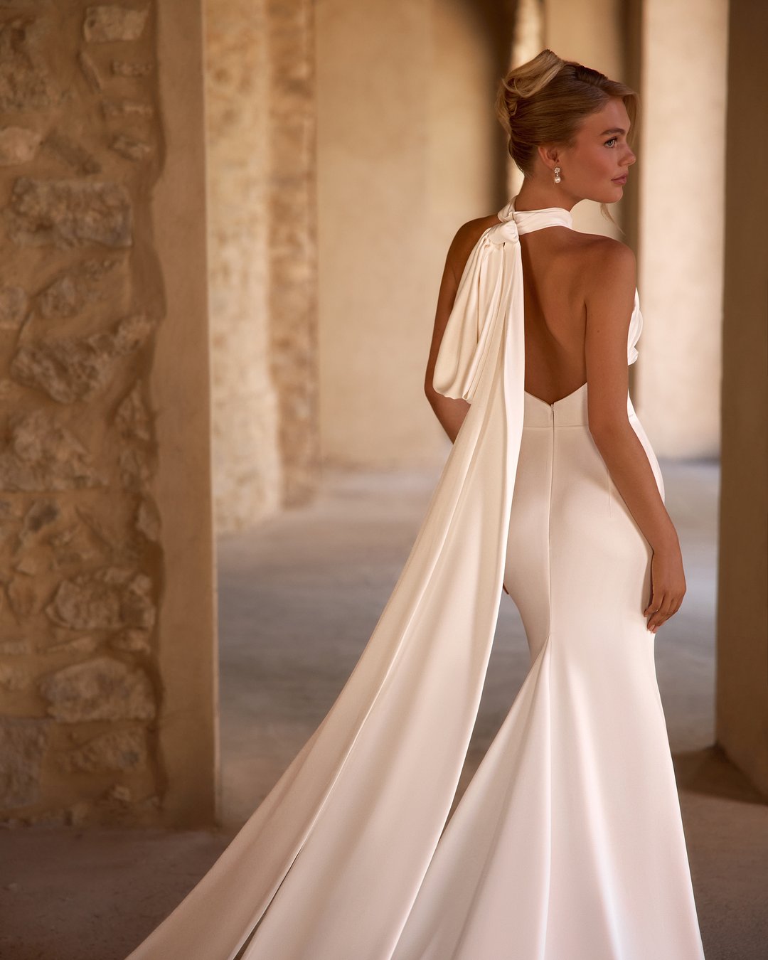 Suknia ślubna Fokuella z kolekcji AnnaSposa to kwintesencja elegancji i klasyki, która zachwyca lekkością i perfekcyjnym dopasowaniem. Jej gładka satyna oraz dekolt halter podkreślają sylwetkę, a wycięte plecy i marszczenia w talii dodają wyjątkowego uroku. Odpinana kokarda oraz tren sprawiają, że każda panna młoda poczuje się niczym prawdziwa księżniczka w tym niezwykłym modelu.