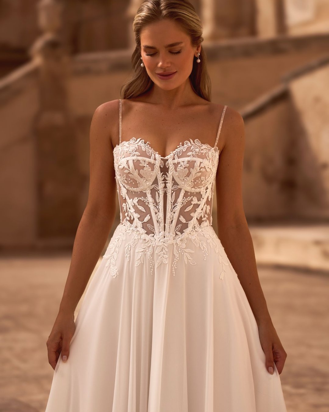 Model Bogdana to romantyczna suknia ślubna o kroju A-line, wykonana z niezwykle lekkiego i zwiewnego muślinu, który pięknie układa się w ruchu. Jej delikatność idzie w parze z elegancją i kobiecością, tworząc stylizację idealną zarówno na ślub w plenerze, jak i elegancką uroczystość w pałacowym stylu.