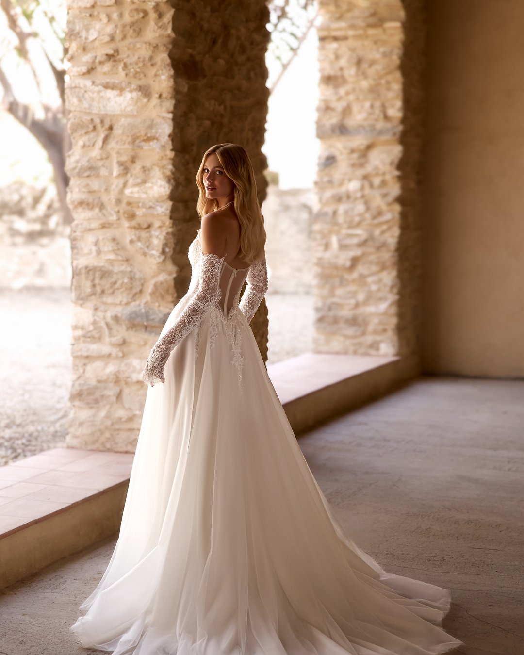 Suknia ślubna Forutina z kolekcji AnnaSposa to romantyczny wybór dla wyjątkowej panny młodej. Jej rozkloszowana linia A, zdobiona koronką francuską, zachwyca przezroczystymi detalami oraz efektownym trenem, natomiast gorsetowy krój z wyciętymi plecami podkreśla sylwetkę, a subtelny rozporek dodaje nuty zmysłowości. Dodatkowe, nakładane rękawy wprowadzają elegancję, sprawiając, że każda chwila w tej sukni będzie niezapomniana.