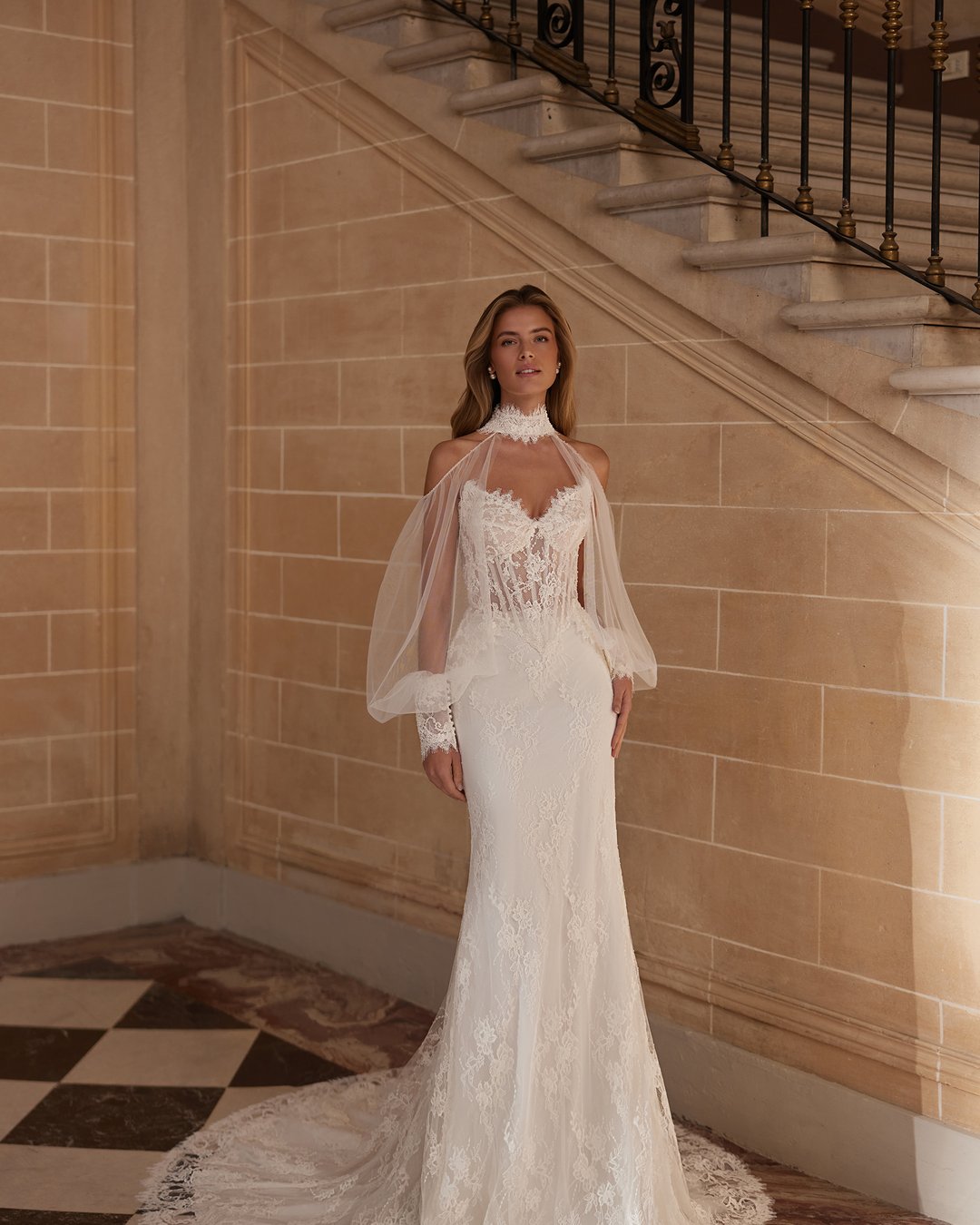 Suknia ślubna Vestira z kolekcji AnnaSposa to kwintesencja elegancji i klasyki, łącząca w sobie dwuczęściowy design z zjawiskowym trenem. Wykonana z delikatnego tiulu i francuskiej koronkowej tkaniny, ozdobiona perłami oraz przezroczystymi nakładanymi rękawami, podkreśla kobiece kształty dzięki gorsetowemu fasonowi i baskince. Idealna dla panien młodych pragnących olśniewać w dniu swojego ślubu.