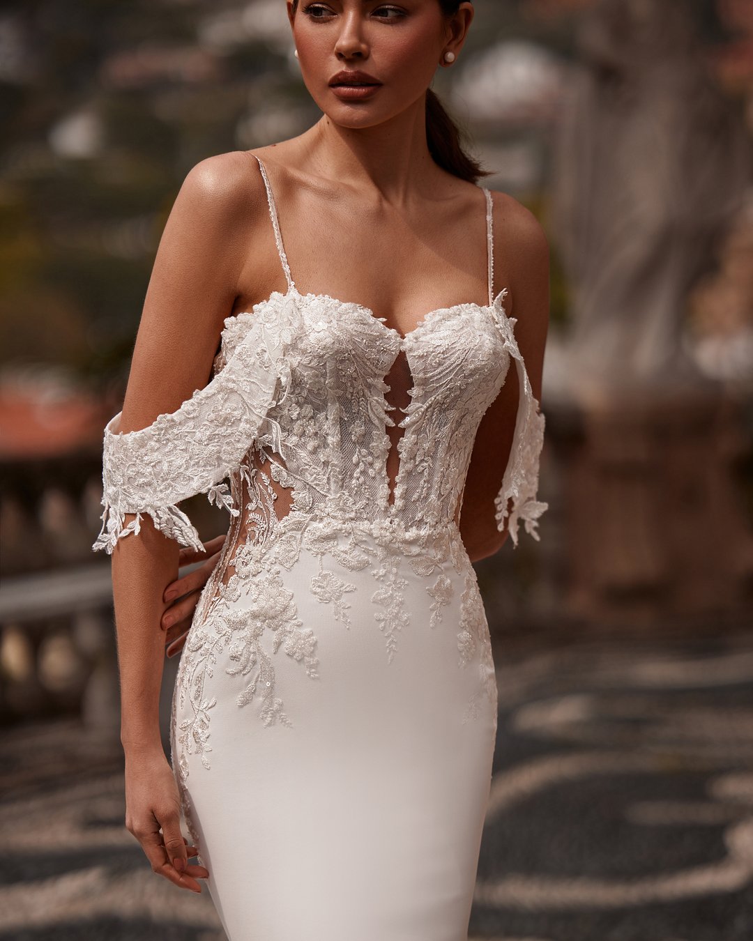 Suknia ślubna Romanta z kolekcji AnnaSposa to doskonały wybór dla eleganckiej panny młodej, która pragnie połączyć klasykę z nowoczesnym stylem. Jej dopasowany krój w formie tuby subtelnie eksponuje sylwetkę, a odkryte plecy i opadające ramiączka dodają romantycznego uroku. Wykonana z delikatnej koronki i krepy, suknię wieńczy efektowny tren, który sprawi, że poczujesz się jak prawdziwa księżniczka w dniu swojego ślubu.