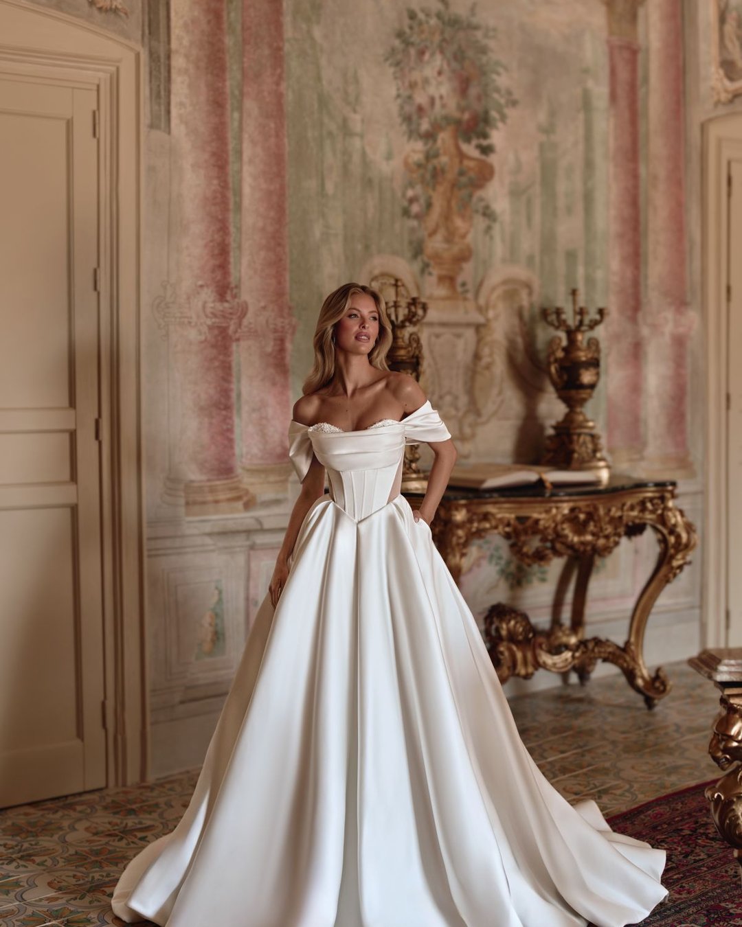 Suknia Toya to wyjątkowa propozycja od Anna Sposa dla miłośniczek klasycznej elegancji. Gładka, wykonana z luksusowej satyny, posiada gorsetowy fason z opadającymi ramiączkami i transparentnymi wstawkami, które dodają subtelnej zmysłowości. Całość uzupełniają błyszczące kryształki, przezroczyste plecy oraz efektowny rozporek.