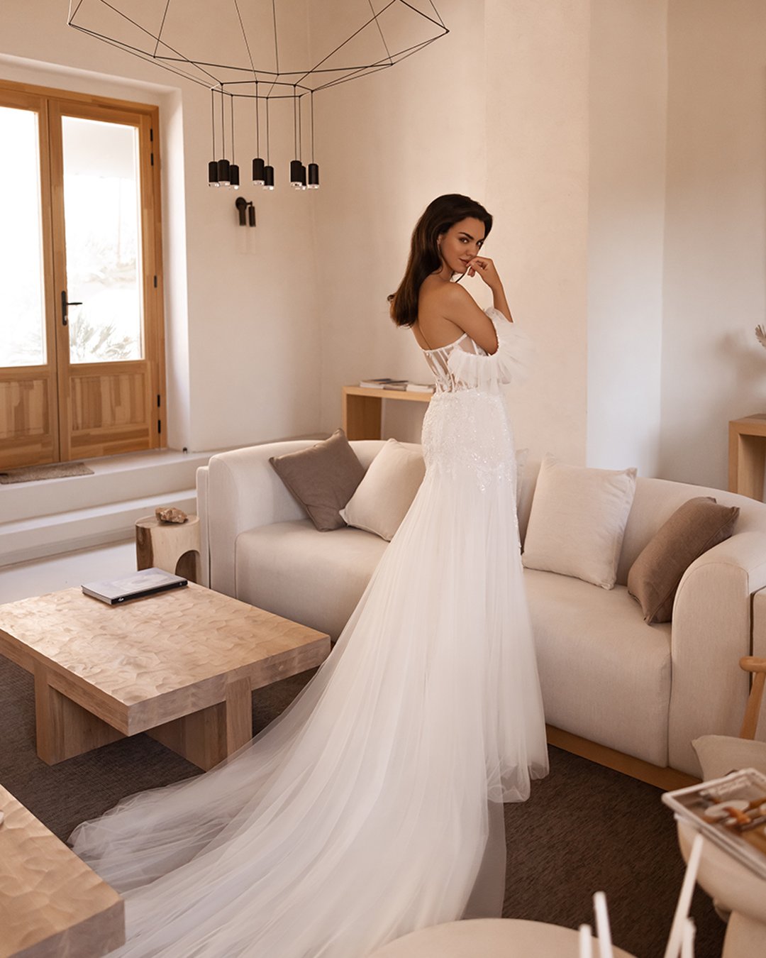 Elegancka suknia o kroju syreny, wykonana z błyszczącej koronki i tiulu brokatowego. Gorsetowa konstrukcja z dopinanymi rękawkami oraz romantyczny tren podkreślają naturalne piękno i dodają subtelnej lekkości. Idealna dla panny młodej szukającej klasyki z nowoczesnym akcentem.