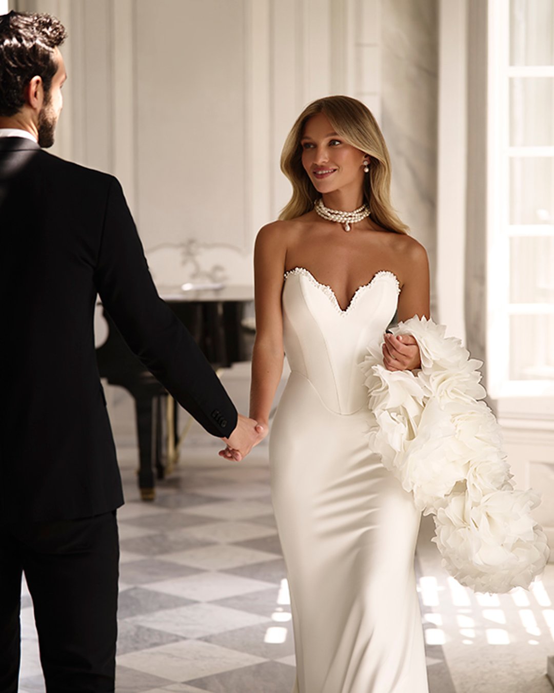 Suknia Uliana od Anna Sposa to esencja współczesnej elegancji z nutą klasyki. Gładka, dopasowana linia z wyraźnym pasem w literę V i gorsetowym topem pięknie podkreśla sylwetkę. Subtelne perełki przy dekolcie oraz spektakularne bolerko z kwiatowymi aplikacjami dodają szyku i oryginalności. To propozycja dla panny młodej, która ceni sobie minimalizm, ale nie boi się wyrazistych detali.