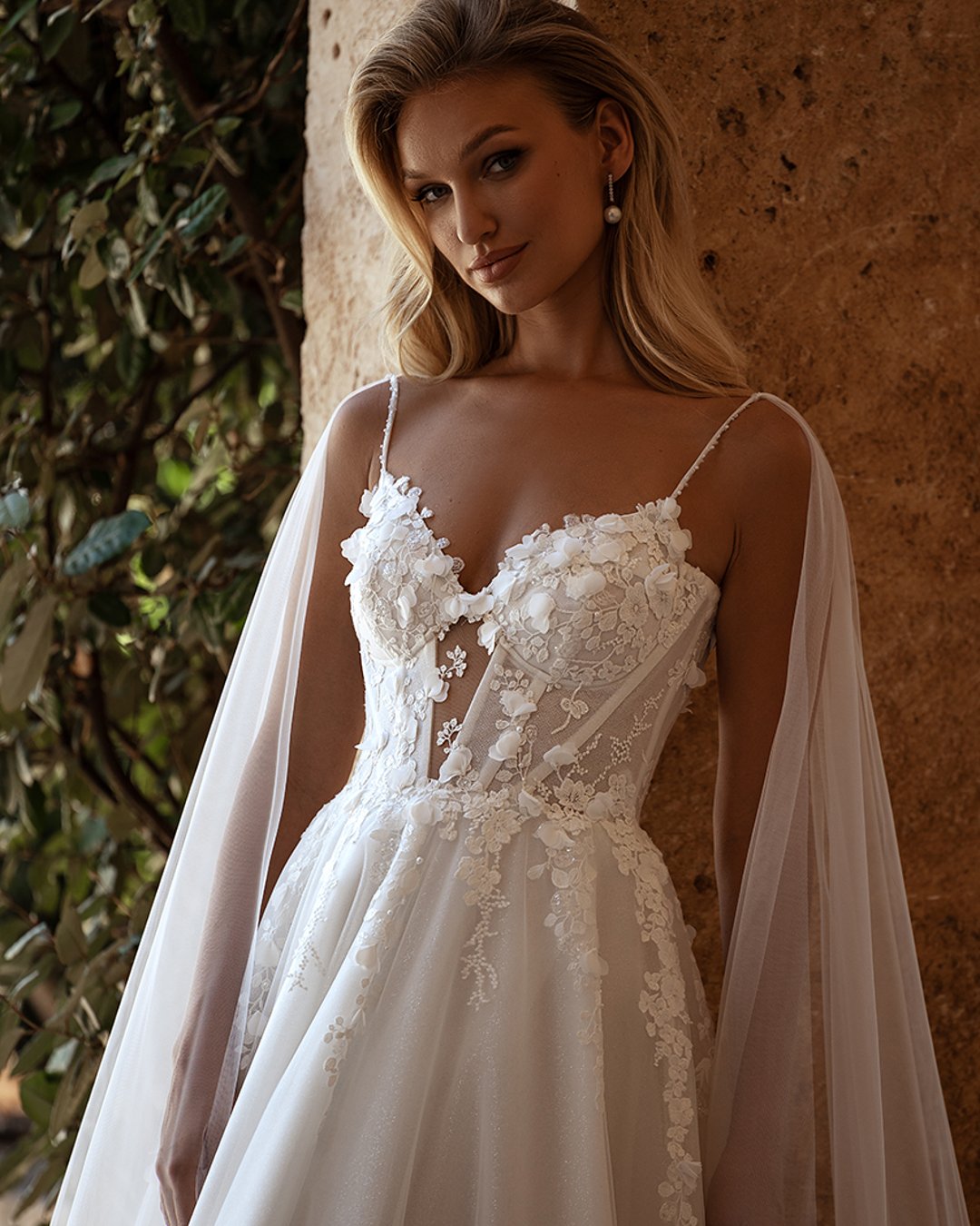 Model Avva, wykonana z lekkiego tiulu i koronki, o kroju litery A z kwiatkami 3D i trenem. Idealna dla panny młodej szukającej elegancji i subtelności.