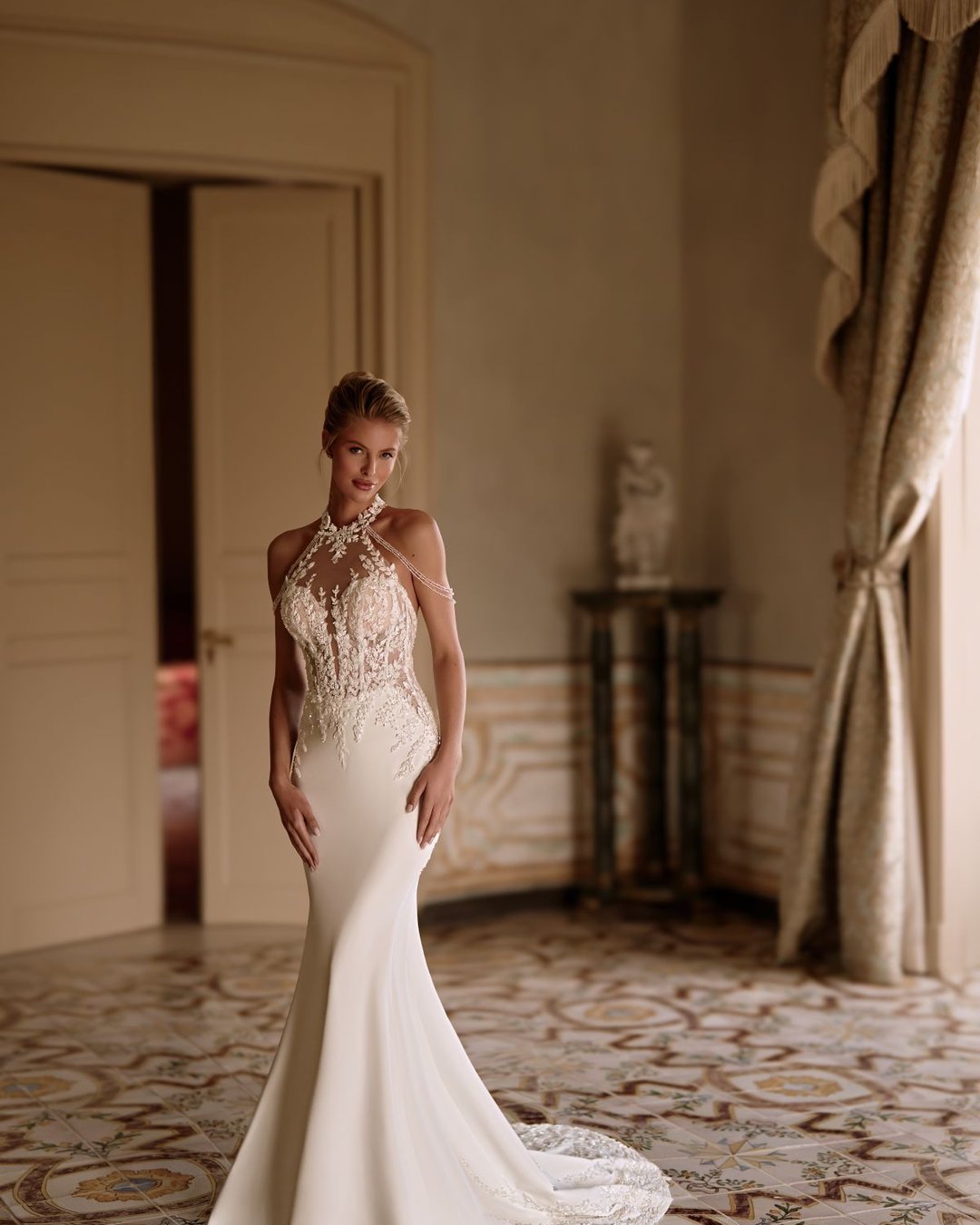 Suknia Sherwood to połączenie klasyki i nowoczesnej elegancji. Zmysłowy halter z opadającymi ramiączkami, przezroczysta koronkowa góra i gładka, wąska spódnica z trenem tworzą efektowną całość. Subtelne zdobienia nadają jej wyjątkowego blasku i lekkości.