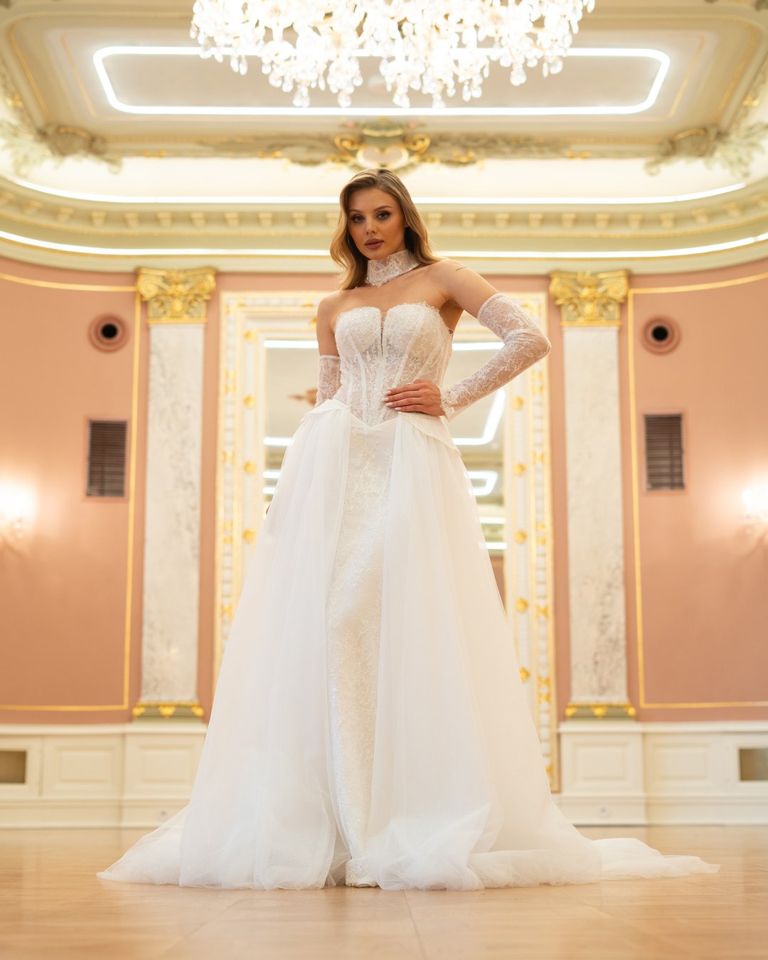 Suknia ślubna Bianca z kolekcji LaLiven to doskonałe połączenie klasyki i nowoczesności, które zachwyca swoją elegancją. Dwuczęściowa konstrukcja w kształcie tuby, ozdobiona francuską koronką i subtelnym trenem, podkreśla sylwetkę, a efektowne nakładane rękawki oraz choker dodają jej wyjątkowego charakteru. Dzięki wąskiej baskince i lśniącemu wykończeniu, Bianca sprawi, że każda panna młoda poczuje się jak prawdziwa gwiazda w dniu swojego ślubu.