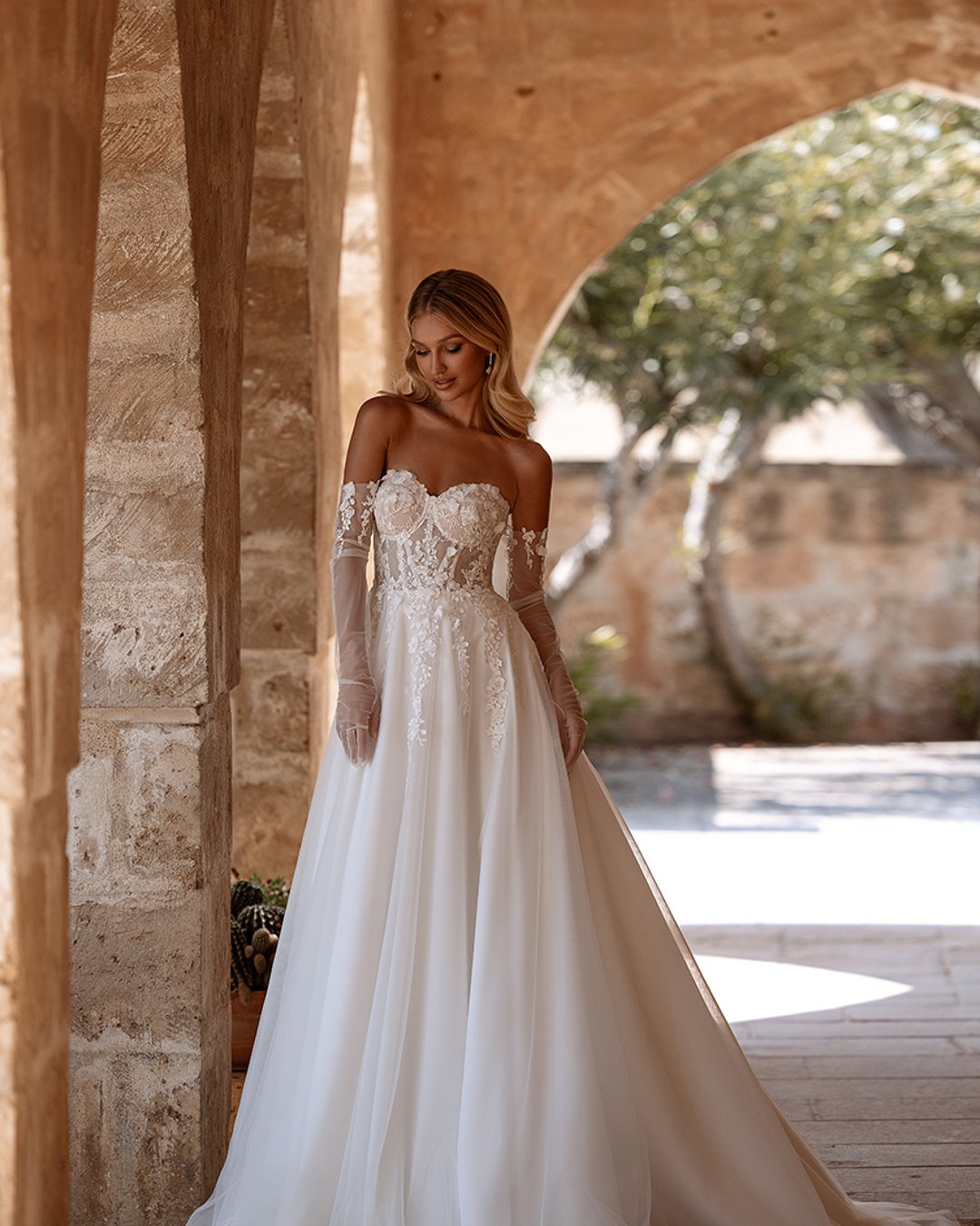 Model Dalarna, o kroju princesski, wykonana z tiulu i koronki 3D, z eleganckimi rękawiczkami i trenem. Idealna dla panny młodej, która pragnie delikatności, elegancji i romantyzmu w swoim wielkim dniu.