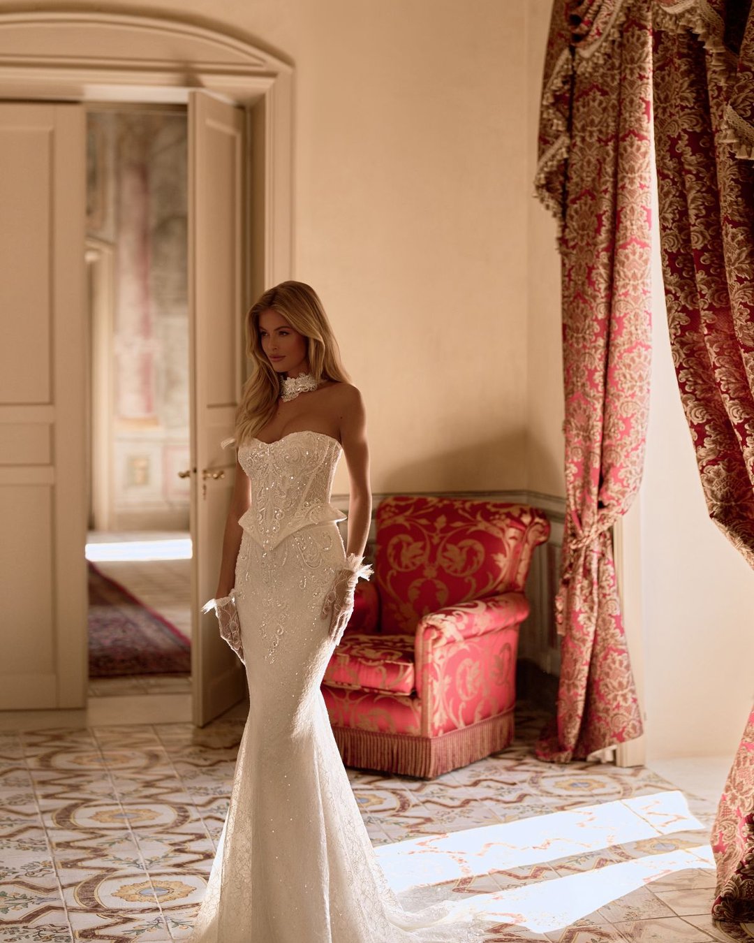 Model Zaphir od Anna Sposa to niezwykle elegancka i dopasowana suknia ślubna o nowoczesnym charakterze. Gorsetowa góra z baskinką i paskiem w literę V subtelnie modeluje talię, a całość wykonana z luksusowej francuskiej koronki nadaje kreacji unikalnego stylu. Tuba o dwuczęściowym efekcie podkreśla sylwetkę, a detale, jak choker i rękawiczki, dodają klasy i oryginalności.