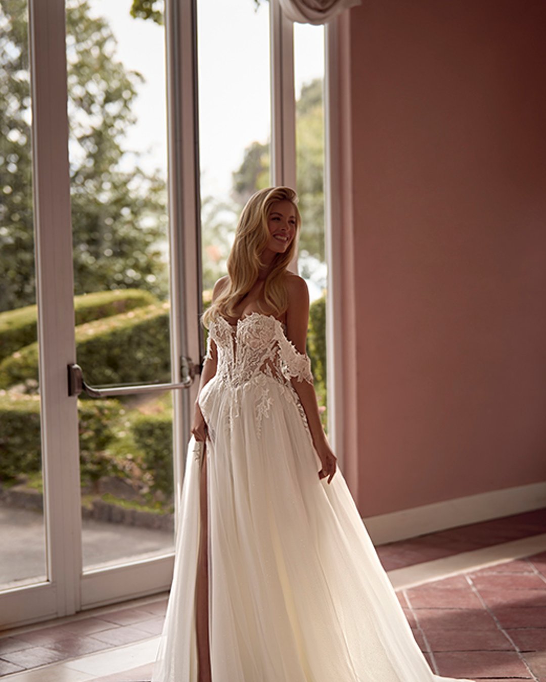 Zmysłowa, romantyczna i pełna lekkości – suknia Virinea to połączenie klasycznej princesski z nowoczesnym charakterem. Transparentny gorset z opadającymi ramiączkami pięknie eksponuje dekolt i ramiona, a delikatna spódnica z tiulu z rozcięciem subtelnie odsłania nogę. Idealna dla Panny Młodej, która marzy o bajkowej, ale wyrazistej stylizacji.