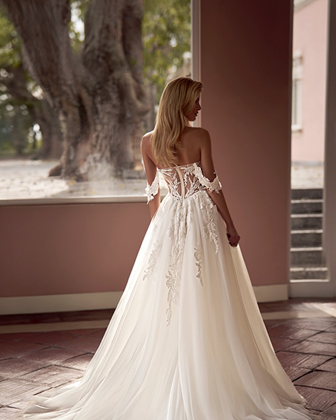 Zmysłowa, romantyczna i pełna lekkości – suknia Virinea to połączenie klasycznej princesski z nowoczesnym charakterem. Transparentny gorset z opadającymi ramiączkami pięknie eksponuje dekolt i ramiona, a delikatna spódnica z tiulu z rozcięciem subtelnie odsłania nogę. Idealna dla Panny Młodej, która marzy o bajkowej, ale wyrazistej stylizacji.