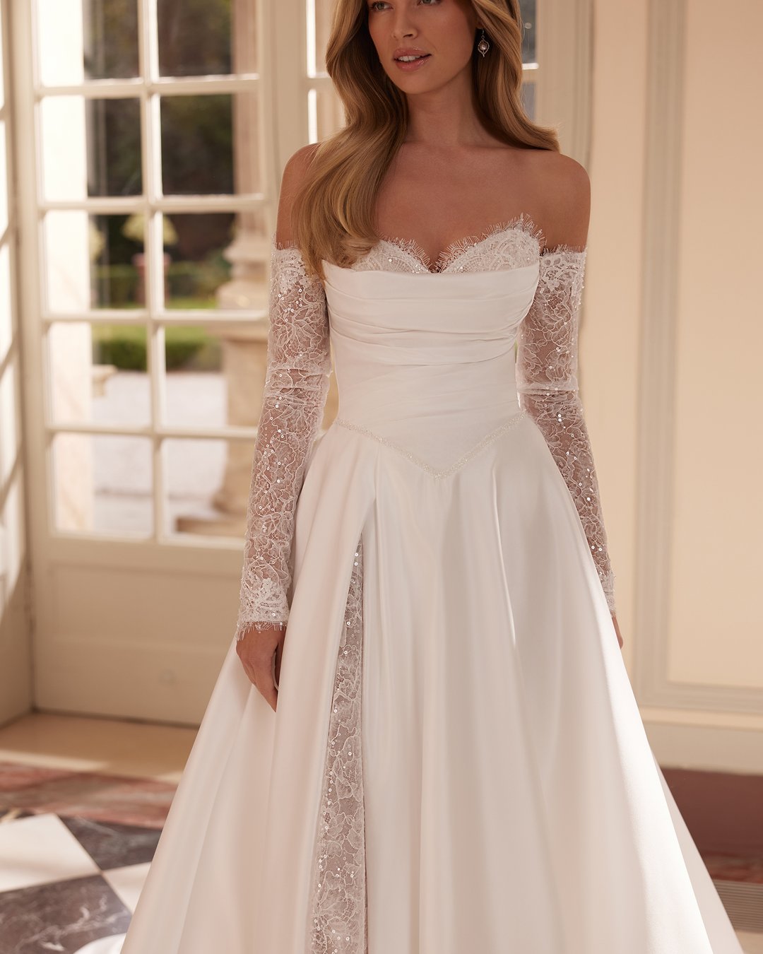 Suknia ślubna Vertalia z kolekcji AnnaSposa to kwintesencja klasycznej elegancji. Jej szeroka spódnica z rozcięciem i efektownym trenem w połączeniu z gorsetowym pasem w kształcie litery V oraz dekoltem serduszko podkreślają kobiecą sylwetkę, a delikatna francuska koronka dodaje całości subtelnego uroku. W tej sukni każda panna młoda poczuje się wyjątkowo w dniu swojego ślubu.