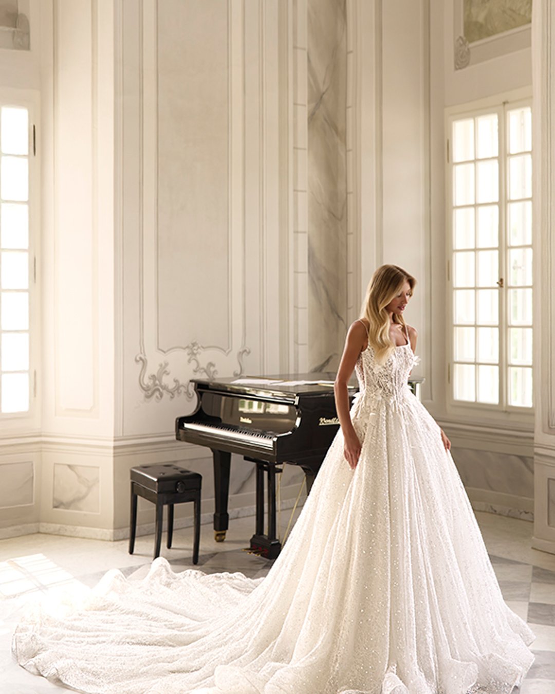 Suknia ślubna Kupelius to olśniewająca princessa z szeroką, błyszczącą spódnicą, zdobiona perełkami i koronką. Na cienkich ramiączkach, z prostym dekoltem i delikatnie prześwitującą górą – elegancja w najczystszej formie.