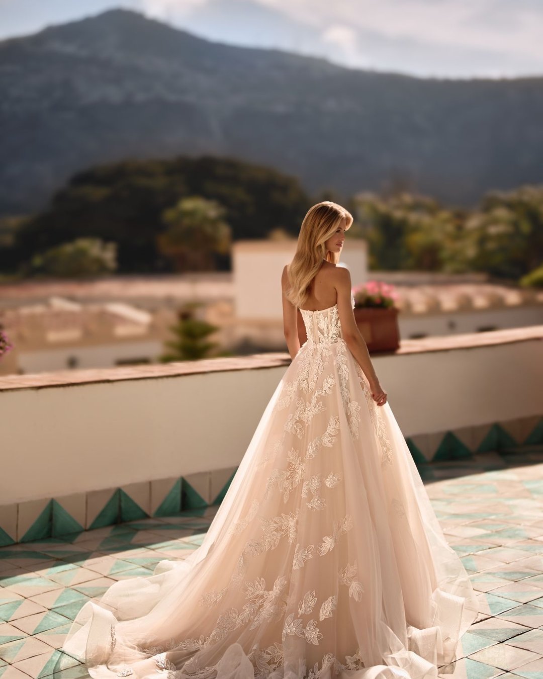 Iltana to romantyczna suknia ślubna z dekoltem halter, wyciętymi plecami i dekoracyjnymi aplikacjami w kształcie liści. Zachwyca szeroką, tiulową spódnicą, delikatnym połyskiem i subtelnym trenem.