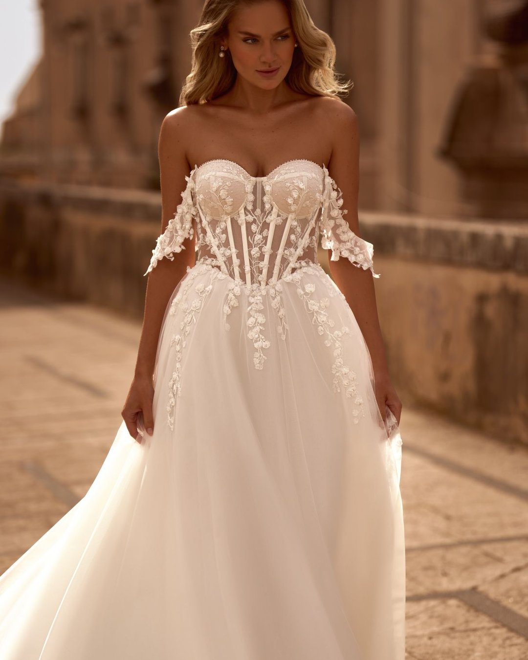 Model Krasyva to romantyczna i niezwykle kobieca suknia ślubna o kroju A-line, która zachwyca swoją delikatnością i subtelnym wykończeniem. Wykonana z lekkiego tiulu, miękko otula sylwetkę, tworząc lekką i zwiewną kompozycję idealną na każdy typ ceremonii – od plenerowego ślubu po elegancką uroczystość w pałacowych wnętrzach.