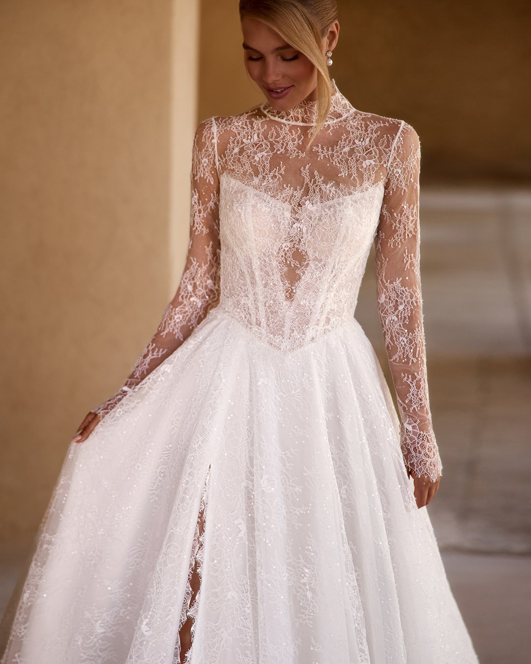Suknia ślubna Sirella z kolekcji AnnaSposa to kwintesencja romantyzmu, łącząca lekkość z elegancją. Jej rozkloszowany krój w linii A, podkreślający sylwetkę dzięki pasowi w kształcie litery V, współgra z delikatnym gorsetem i przezroczystym bolerkiem, natomiast francuska koronka dodaje jej wyjątkowego blasku. Z trenem, który subtelnie podkreśla każdy krok, Sirella sprawi, że każda panna młoda poczuje się jak prawdziwa księżniczka w swoim wyjątkowym dniu.
