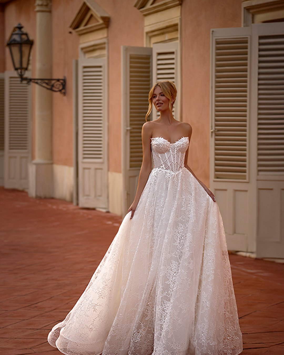 Elegancka suknia ślubna Lazurina zachwyca romantyczną linią A, pełną koronkowych detali i subtelnego blasku. Gorsetowy fason w połączeniu z dopinanym bolerkiem tworzy efektowną, a zarazem delikatną stylizację. To idealna propozycja dla Panny Młodej, która ceni klasykę w nowoczesnym wydaniu...