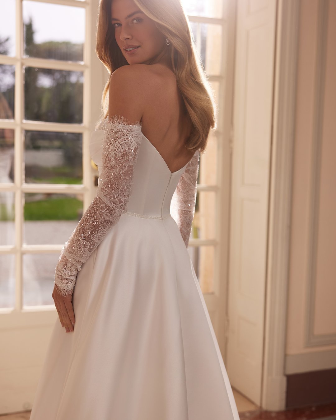 Suknia ślubna Vertalia z kolekcji AnnaSposa to kwintesencja klasycznej elegancji. Jej szeroka spódnica z rozcięciem i efektownym trenem w połączeniu z gorsetowym pasem w kształcie litery V oraz dekoltem serduszko podkreślają kobiecą sylwetkę, a delikatna francuska koronka dodaje całości subtelnego uroku. W tej sukni każda panna młoda poczuje się wyjątkowo w dniu swojego ślubu.