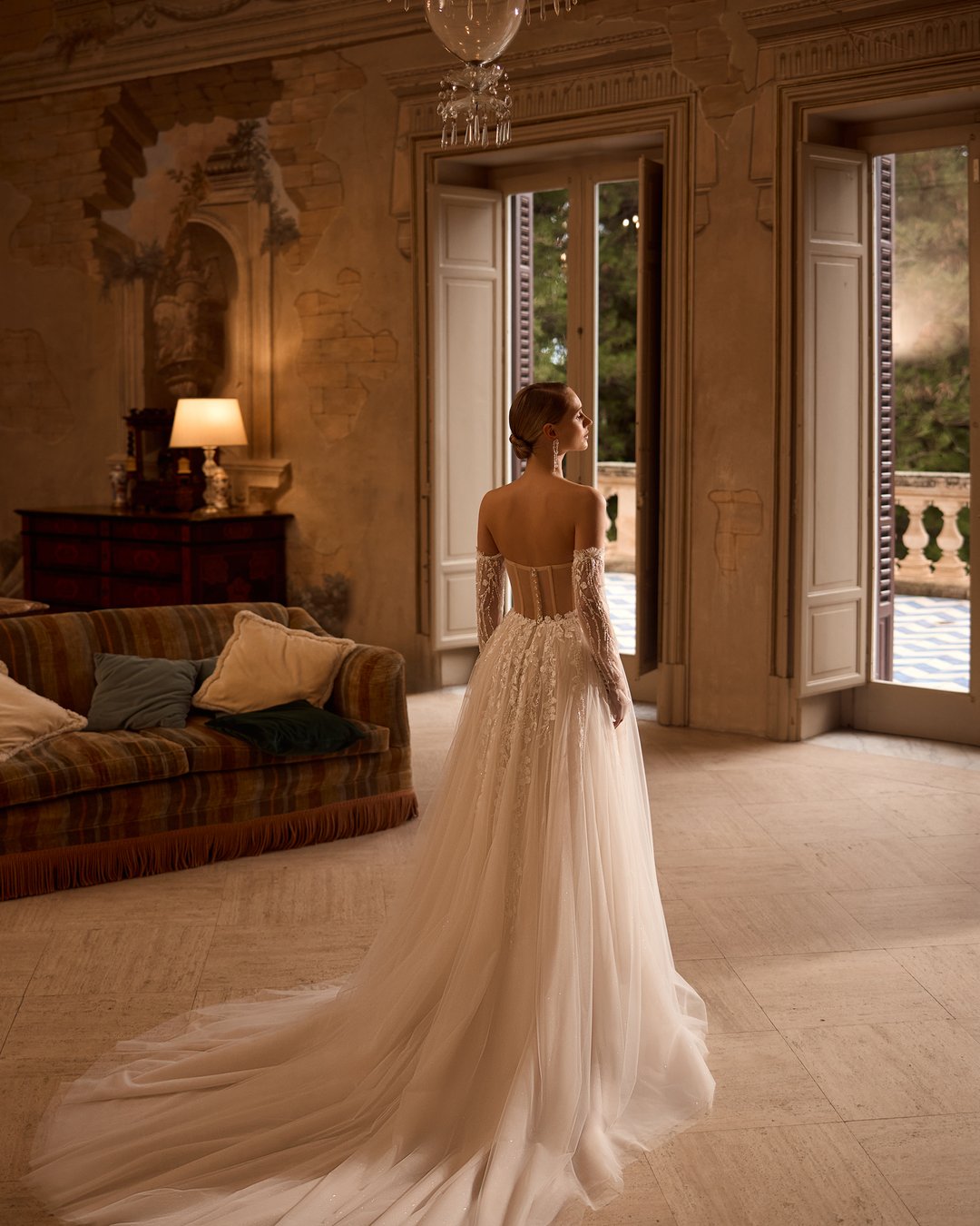 Suknia ślubna 5831 z kolekcji Elizabeth Passion łączy nowoczesny design z romantycznym wyrafinowaniem. Przezroczysta góra ozdobiona delikatną koronką i kwiatowymi aplikacjami, w połączeniu z szeroką, tiulową spódnicą, tworzy niepowtarzalny efekt, który zachwyca blaskiem. Nakładane rękawy dodają całości subtelności, sprawiając, że każda panna młoda poczuje się jak prawdziwa królewna w tym wyjątkowym dniu.