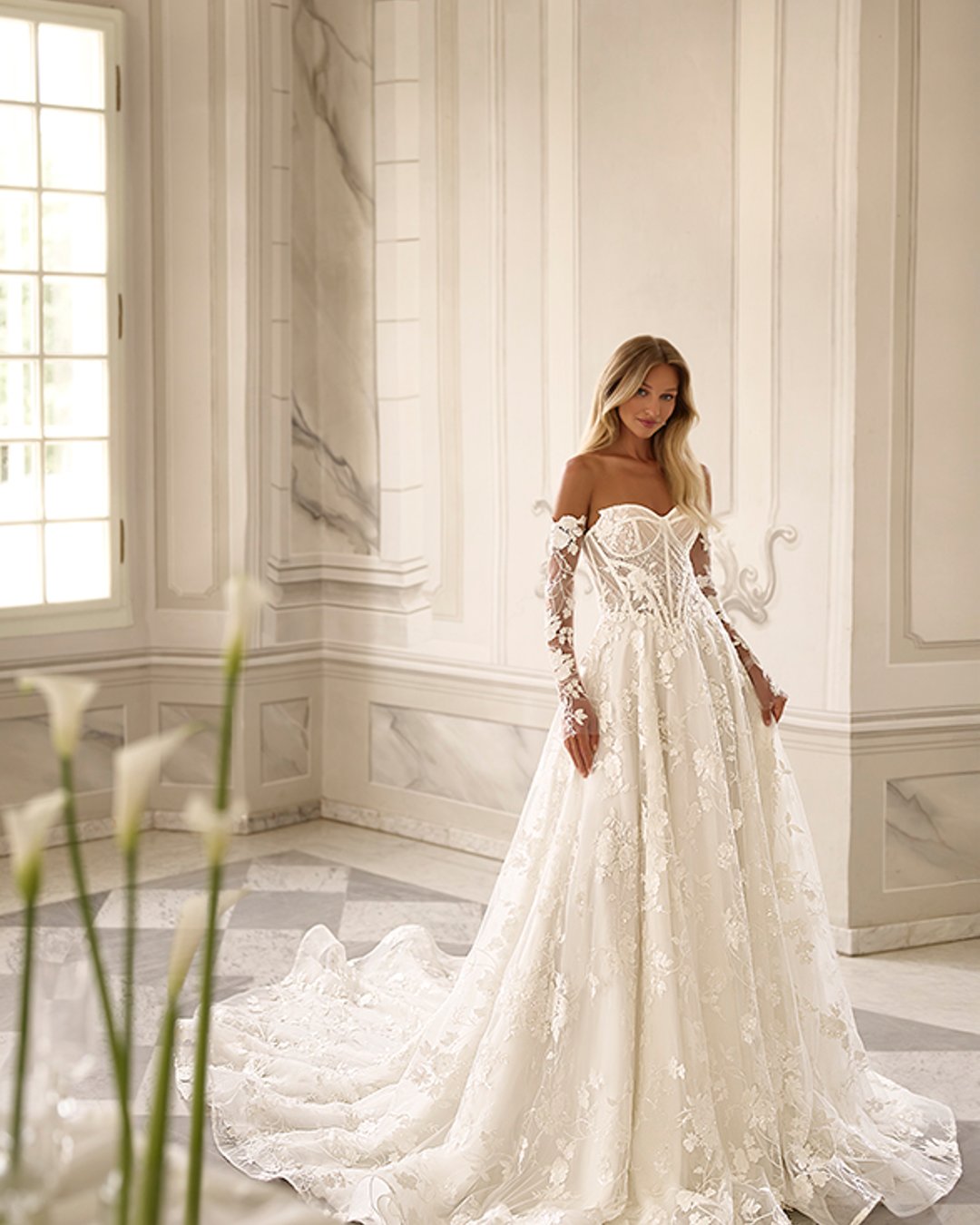 Subtelna suknia Reinbow zachwyca lekkością, romantycznymi kwiatowymi zdobieniami i nowoczesnym krojem w linii A. Gorsetowa góra, przezroczyste detale oraz opcjonalne rękawy tworzą stylową i kobiecą całość.