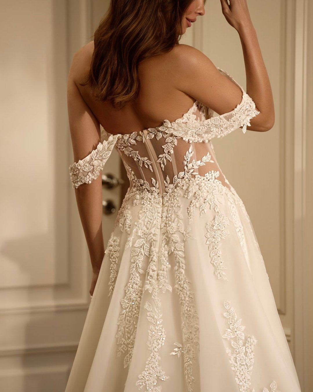 Suknia o linii A, zachwycająca swoją delikatnością i romantycznym charakterem. Gorsetowa góra wykonana z transparentnego tiulu, ręcznie zdobiona misteryjną koronką w motywy roślinne. Przezroczyste boki optycznie modelują sylwetkę, pięknie ją podkreślając.
