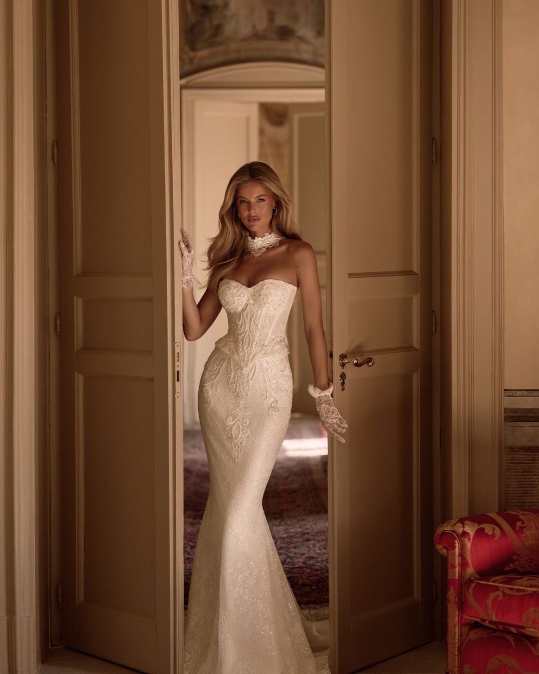 Model Zaphir od Anna Sposa to niezwykle elegancka i dopasowana suknia ślubna o nowoczesnym charakterze. Gorsetowa góra z baskinką i paskiem w literę V subtelnie modeluje talię, a całość wykonana z luksusowej francuskiej koronki nadaje kreacji unikalnego stylu. Tuba o dwuczęściowym efekcie podkreśla sylwetkę, a detale, jak choker i rękawiczki, dodają klasy i oryginalności.