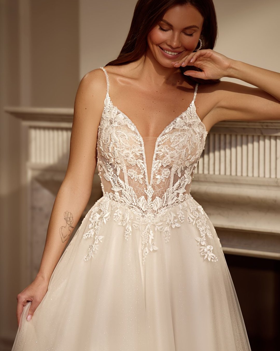 Zjawiskowa suknia w linii A na cienkich, delikatnych ramiączkach. Góra sukni wykonana z transparentnego tiulu zdobionego ręcznie wyszywaną koronką. Głęboki dekolt w kształcie litery V subtelnie eksponuje sylwetkę, a pięknie wycięte, koronkowe plecy dodają sukni romantyzmu i lekkości.