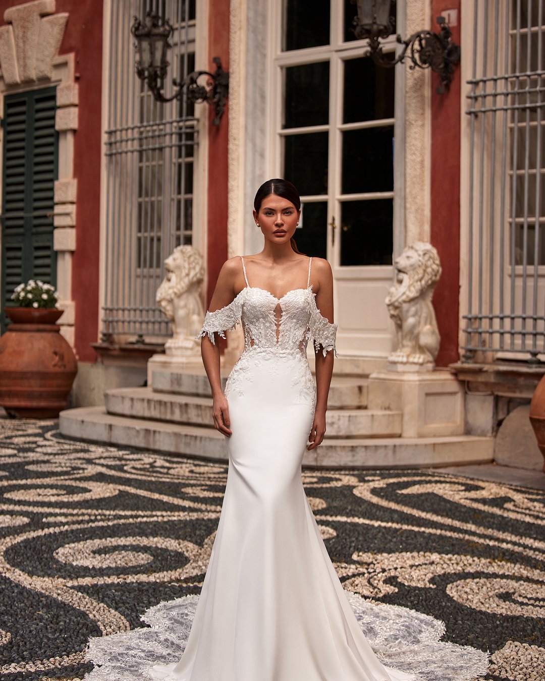 Suknia ślubna Romanta z kolekcji AnnaSposa to doskonały wybór dla eleganckiej panny młodej, która pragnie połączyć klasykę z nowoczesnym stylem. Jej dopasowany krój w formie tuby subtelnie eksponuje sylwetkę, a odkryte plecy i opadające ramiączka dodają romantycznego uroku. Wykonana z delikatnej koronki i krepy, suknię wieńczy efektowny tren, który sprawi, że poczujesz się jak prawdziwa księżniczka w dniu swojego ślubu.