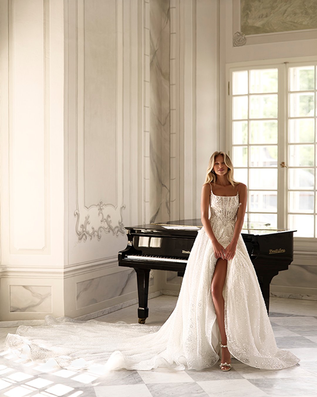 Suknia ślubna Kupelius to olśniewająca princessa z szeroką, błyszczącą spódnicą, zdobiona perełkami i koronką. Na cienkich ramiączkach, z prostym dekoltem i delikatnie prześwitującą górą – elegancja w najczystszej formie.