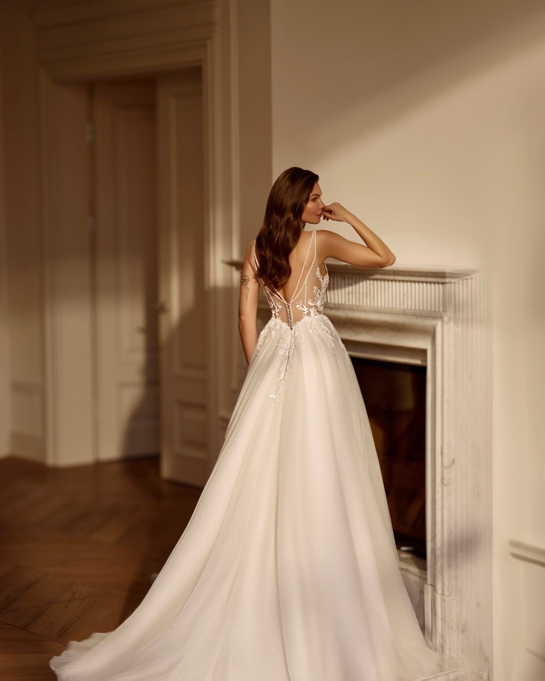 Zjawiskowa suknia w linii A na cienkich, delikatnych ramiączkach. Góra sukni wykonana z transparentnego tiulu zdobionego ręcznie wyszywaną koronką. Głęboki dekolt w kształcie litery V subtelnie eksponuje sylwetkę, a pięknie wycięte, koronkowe plecy dodają sukni romantyzmu i lekkości.