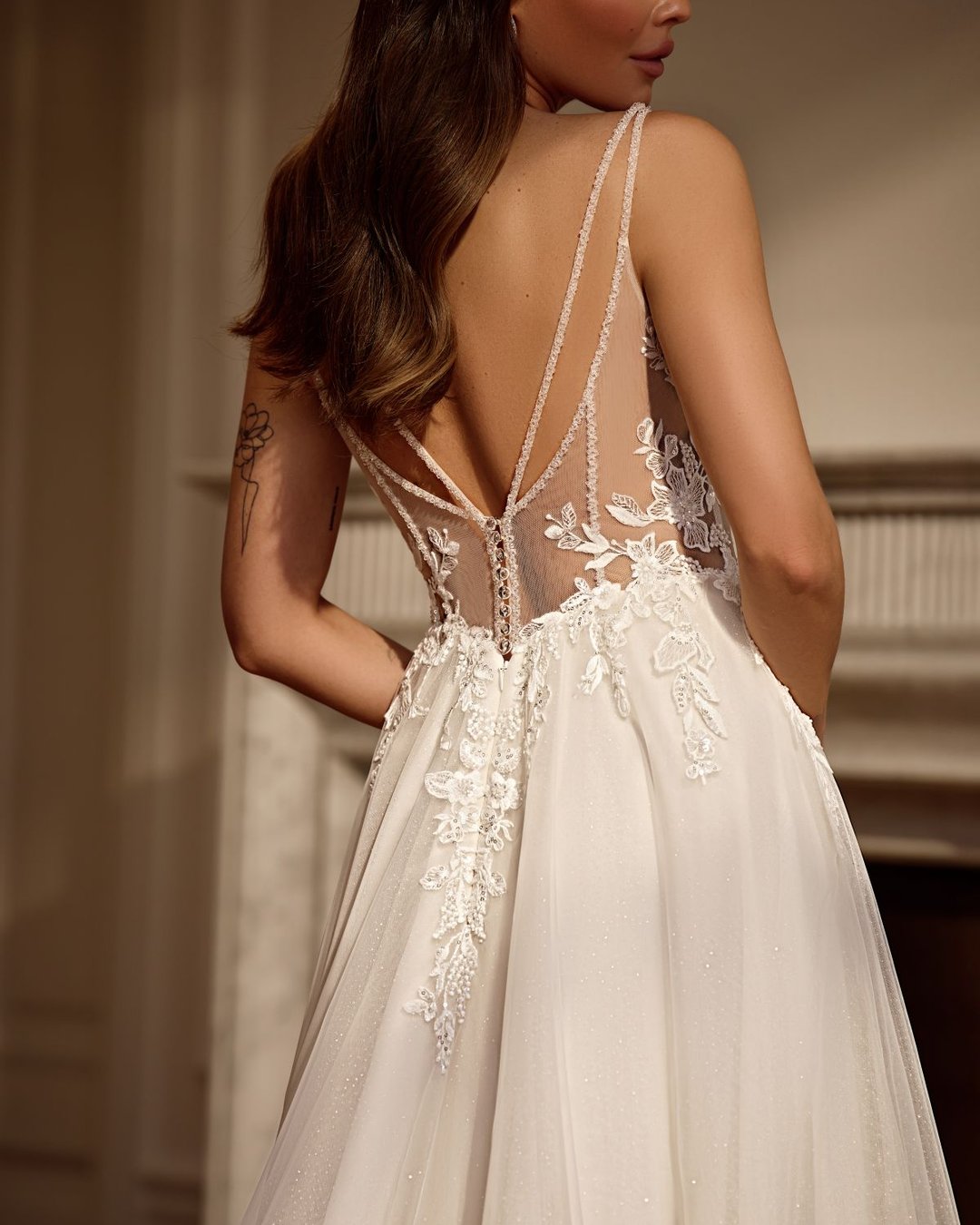 Zjawiskowa suknia w linii A na cienkich, delikatnych ramiączkach. Góra sukni wykonana z transparentnego tiulu zdobionego ręcznie wyszywaną koronką. Głęboki dekolt w kształcie litery V subtelnie eksponuje sylwetkę, a pięknie wycięte, koronkowe plecy dodają sukni romantyzmu i lekkości.