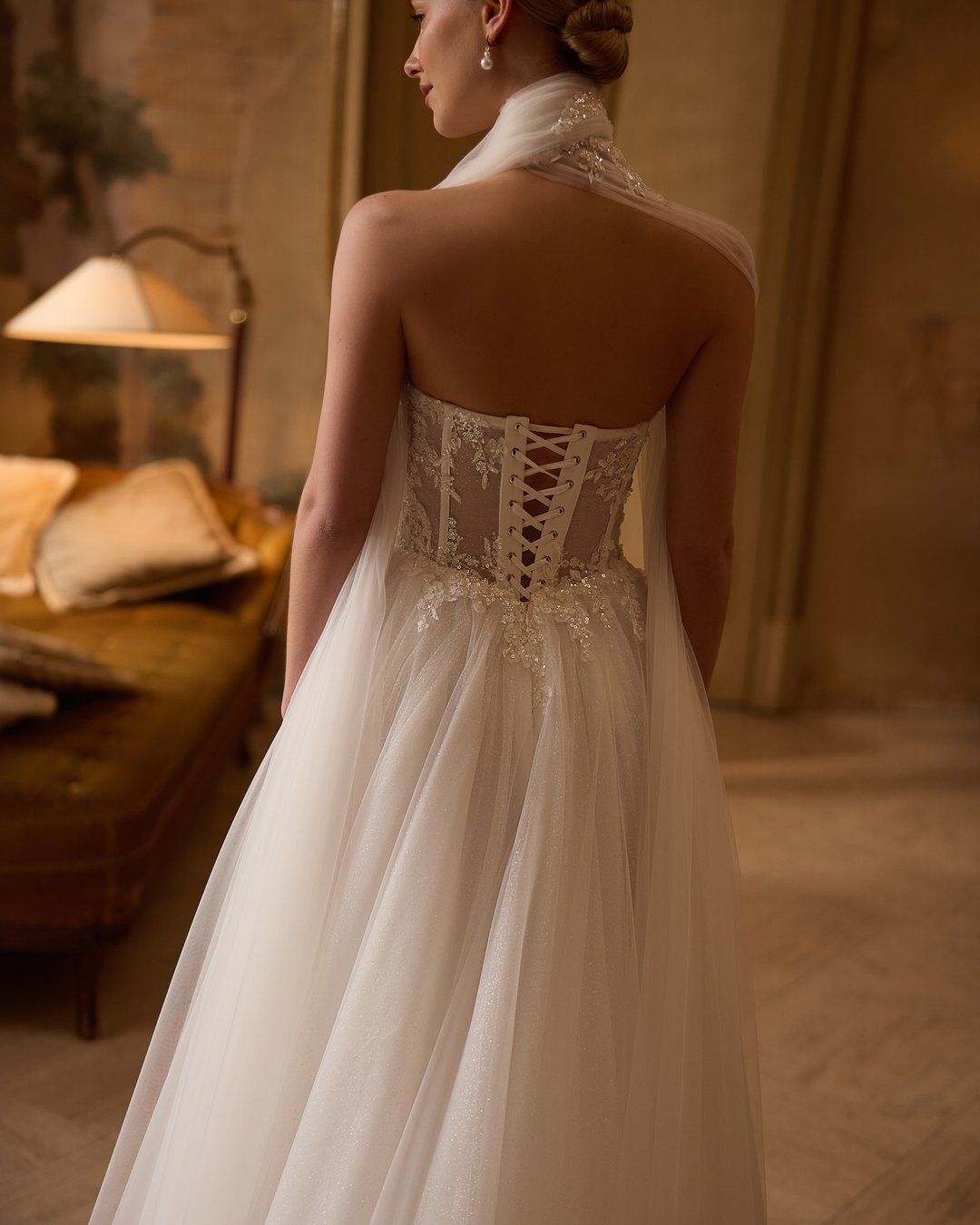 Suknia ślubna 5806 z kolekcji Elizabeth Passion to prawdziwe dzieło sztuki, które łączy nowoczesny styl z romantycznym wdziękiem. Szeroka spódnica z tiulu i koronki, ozdobiona subtelnymi kwiatowymi detalami, w połączeniu z gorsetową górą i eleganckim chokerem, podkreśla sylwetkę, a długi tren dodaje majestatyczności. Ta niezwykła suknia z pasem w kształcie litery V wprowadzi każdą pannę młodą w bajkowy świat miłości i elegancji.