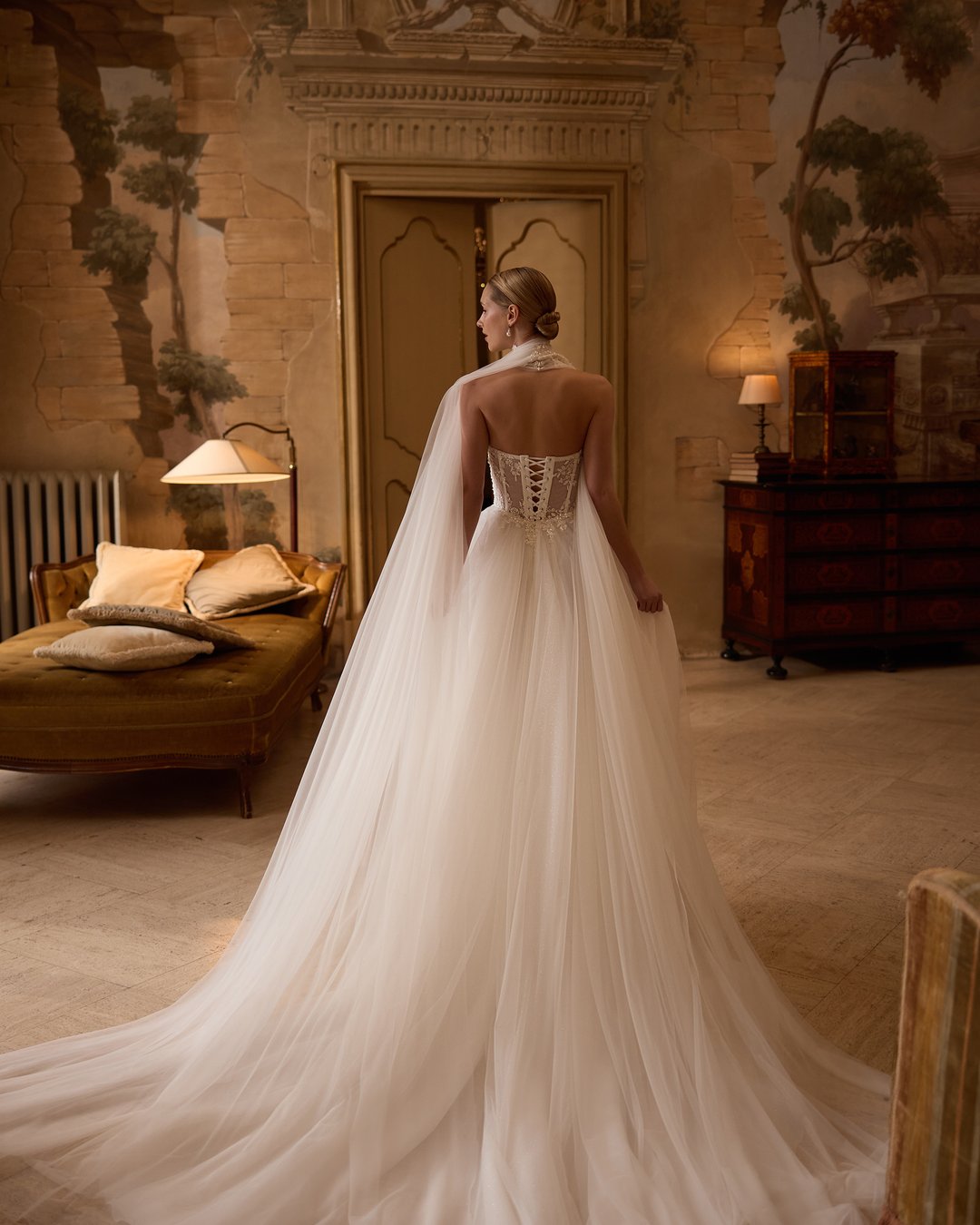 Suknia ślubna 5806 z kolekcji Elizabeth Passion to prawdziwe dzieło sztuki, które łączy nowoczesny styl z romantycznym wdziękiem. Szeroka spódnica z tiulu i koronki, ozdobiona subtelnymi kwiatowymi detalami, w połączeniu z gorsetową górą i eleganckim chokerem, podkreśla sylwetkę, a długi tren dodaje majestatyczności. Ta niezwykła suknia z pasem w kształcie litery V wprowadzi każdą pannę młodą w bajkowy świat miłości i elegancji.