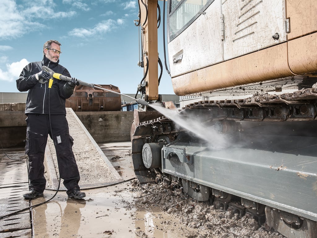 Worker pressure washing mud off an excavator